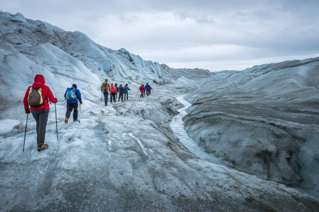 Tourists hiking with poles on the icy surface of the Greenland icecap near Kangerlussuaq, showcasing the stark beauty and rugged terrain of the Arctic region.