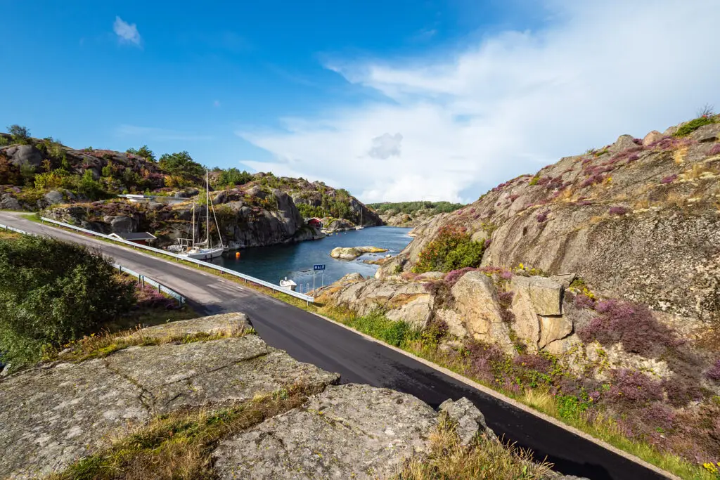 Scenic view of the bridge connecting Orust and Malön islands in Sweden, showcasing rocky landscapes and coastal flora under a clear blue sky.