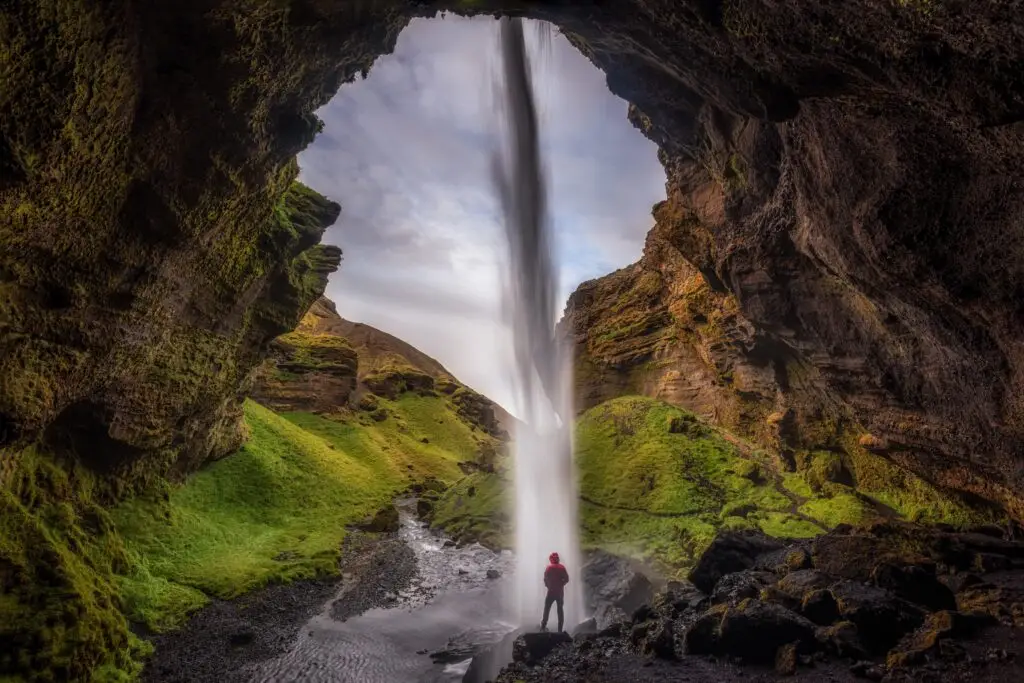 Tourist observing the majestic waterfall from within a cave in Scandinavia, highlighting the unique natural beauty and adventure tourism in the region.