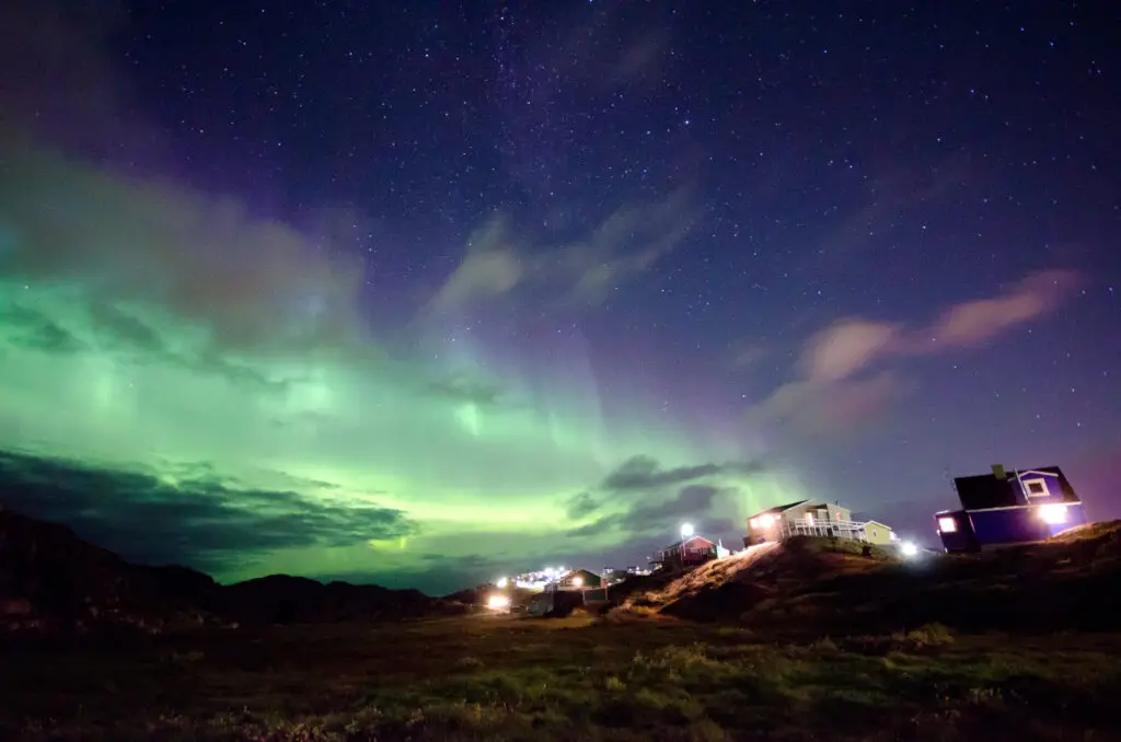 Stunning view of the Northern Lights in Greenland, illuminating the night sky above a small village with colorful houses