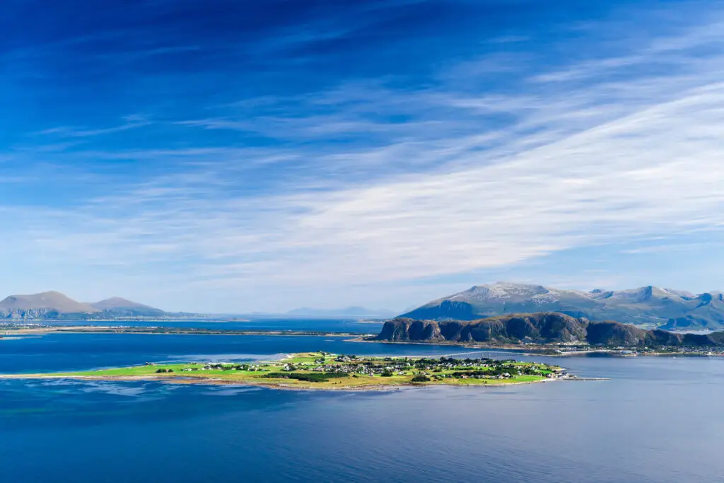 Aerial view of Giske Island in Norway showcasing lush green landscapes during summer with clear blue waters and mountainous backdrop.