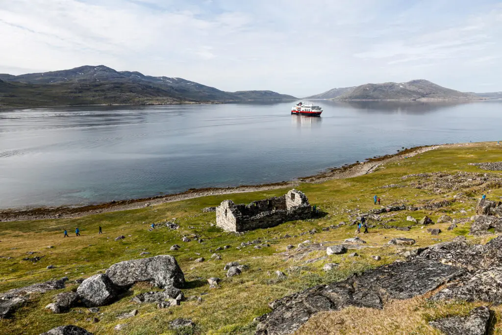 Tourists exploring the ancient Hvalsey Church ruins near a calm fjord with a cruise ship in the background in South Greenland