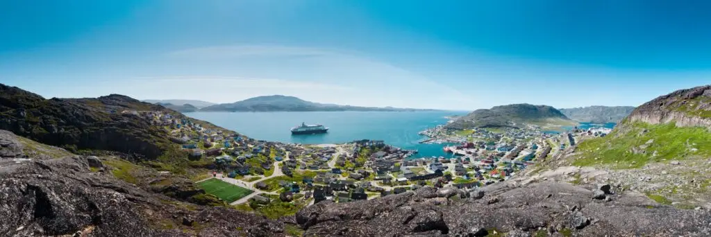 Panoramic view of Qaqortoq, Greenland coastline with colorful houses and a cruise ship sailing in the sea