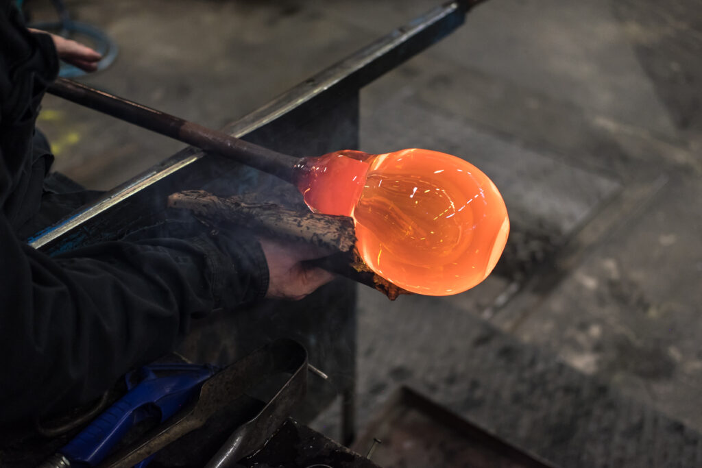 Glassblowing in Kosta, Sweden: Artisan shaping a glowing molten glass blob on a spinning iron tube at a traditional glassworks, demonstrating a unique Scandinavian craft.