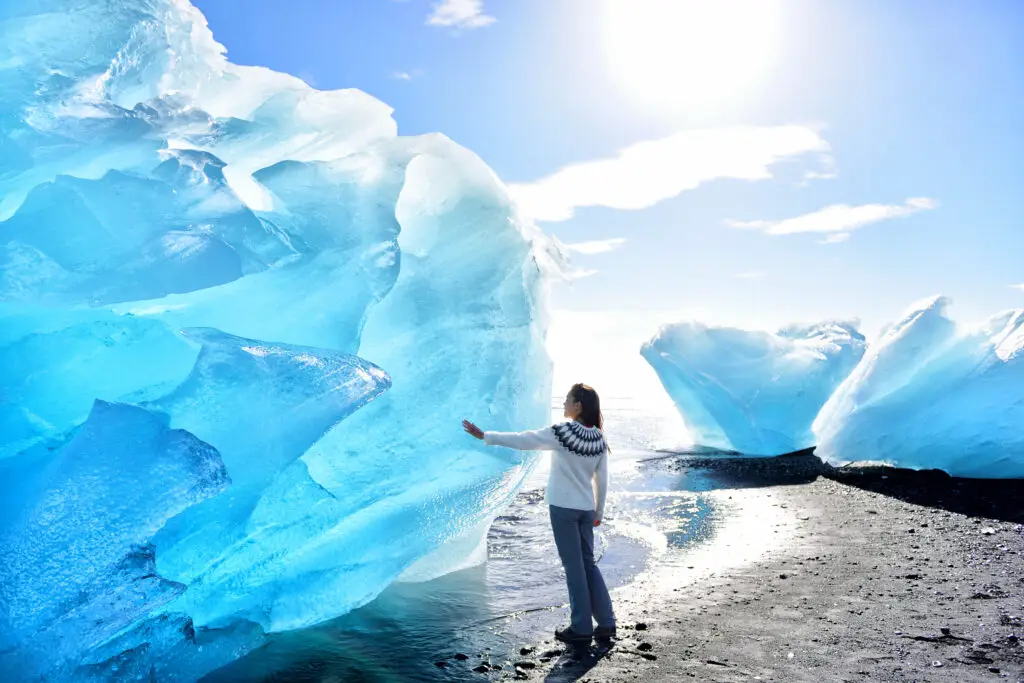 Tourist in Icelandic sweater admiring large blue icebergs at Diamond Beach, near Jokulsarlon Glacier Lagoon in Iceland