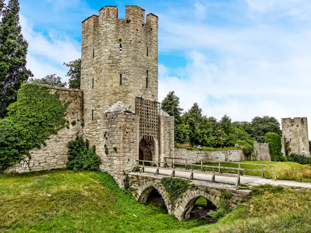 Summer view of Visborg Castle entrance with a stone bridge in Visby, Gotland, Sweden, showcasing medieval architecture and lush greenery.