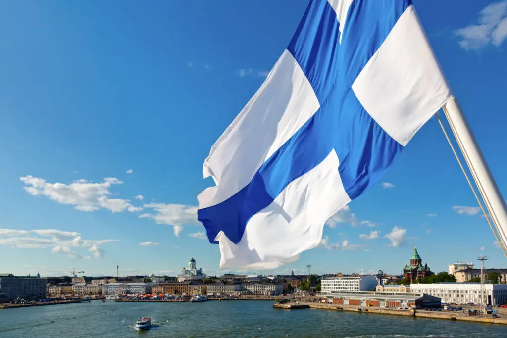 Finnish flag waving over Helsinki skyline with clear blue sky and sea, highlighting Finland's capital cityscape and vibrant urban tourism.