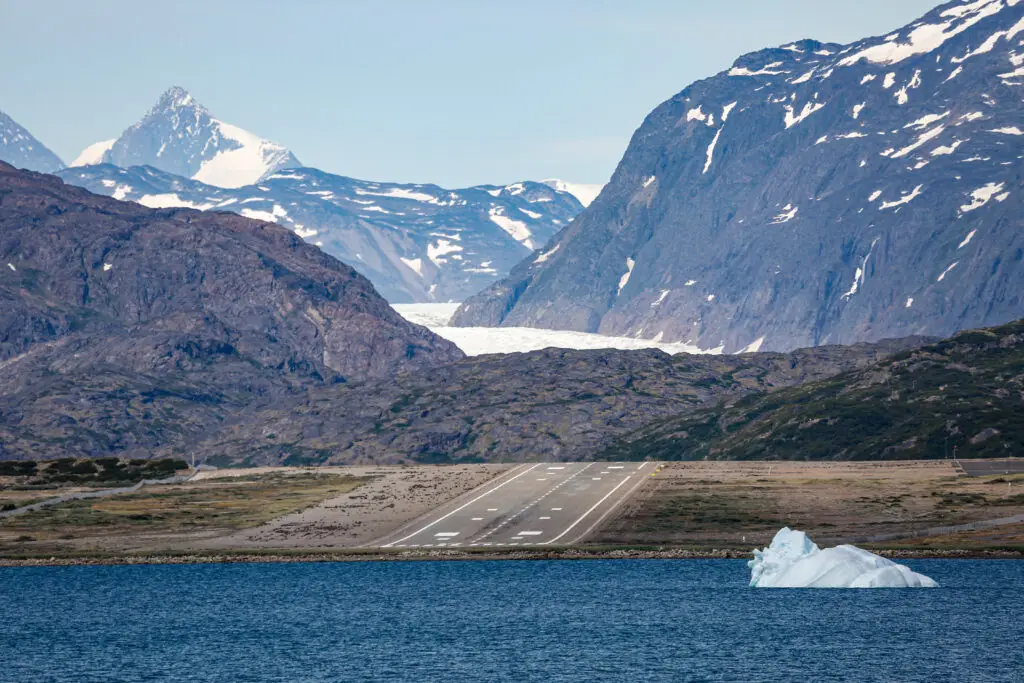 View of Narsarsuaq Airport runway with a backdrop of icebergs and snow-capped mountains in Southwestern Greenland, highlighting a unique Arctic travel destination.