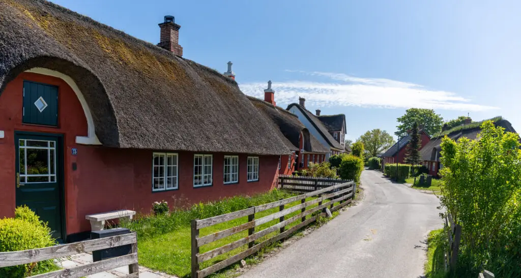 Picturesque village street showcasing traditional Danish thatched-roof houses painted in vibrant red and green in Nordby, Fano Island, ideal for cultural tourism in Scandinavia.