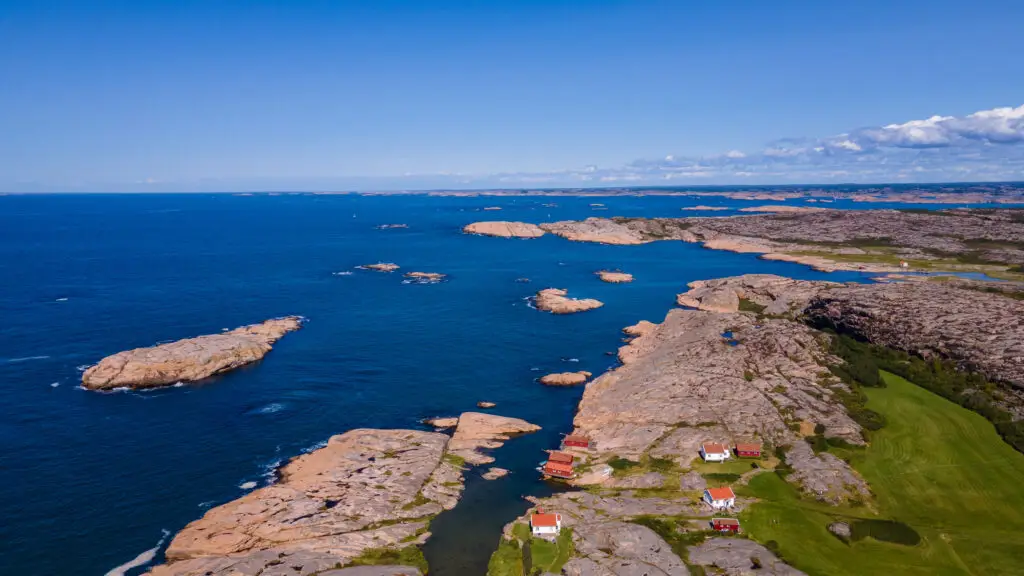 Aerial view of a scenic coastline in Scandinavia with rugged cliffs and traditional red houses, highlighting the beauty of Scandinavian landscape and culture for tourism.
