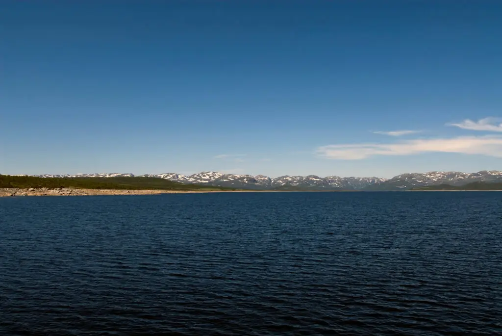 Panoramic view of Møsvatn lake with distant snow-covered mountains in Hardangervidda, Norway, ideal for serene nature tours.