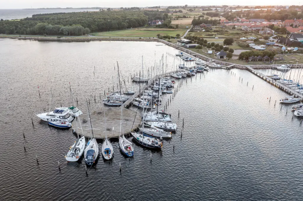 Aerial view of Marstal harbor in Scandinavia during sunset, showcasing numerous moored yachts and the serene coastal landscape.