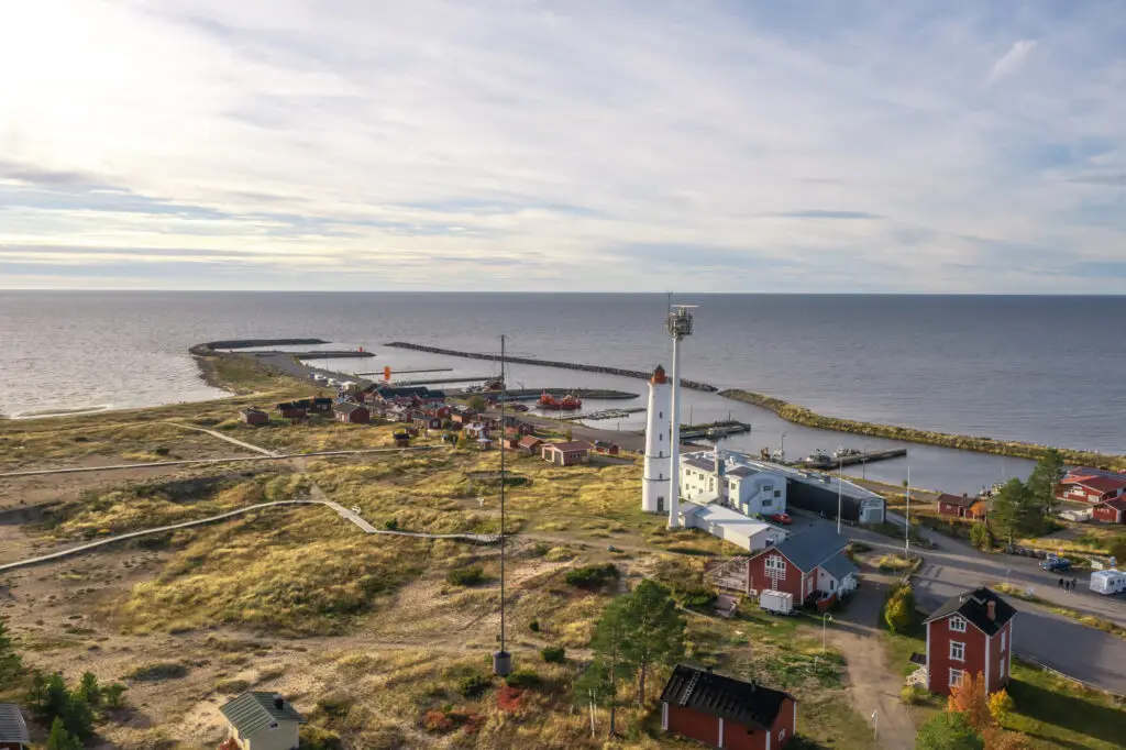 Aerial view of Marjaniemi Lighthouse and surrounding fishing village in Hailuoto, Finland, showcasing scenic coastline and autumn landscape on a sunny day.