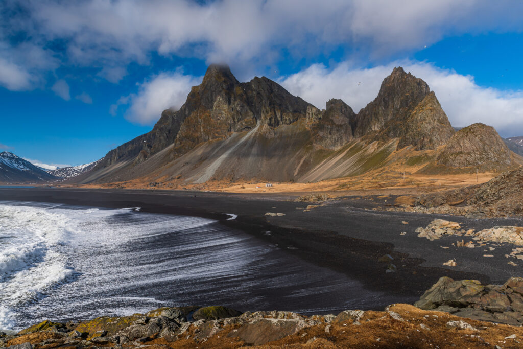 Dramatic view of Hvalnes Peninsula in South Iceland, featuring rugged cliffs and a black sand beach with frothy sea waves.