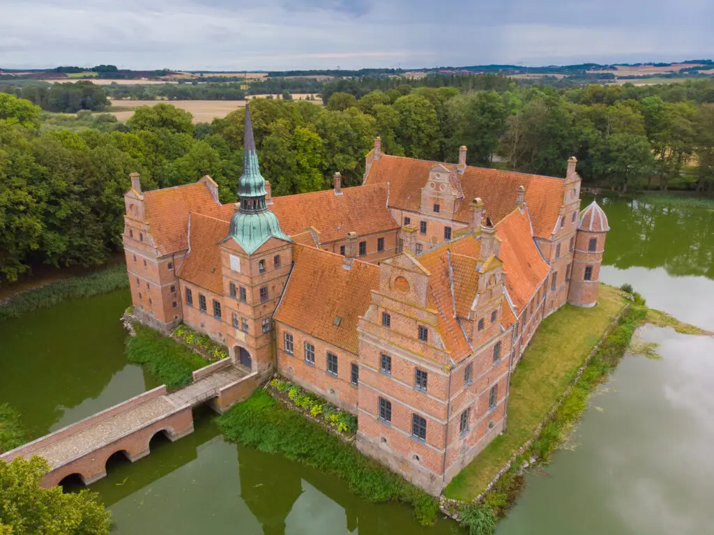 Aerial view of Rosenholm Castle in Denmark surrounded by lush greenery and a reflective moat, showcasing Scandinavian historic architecture and tourism attraction.