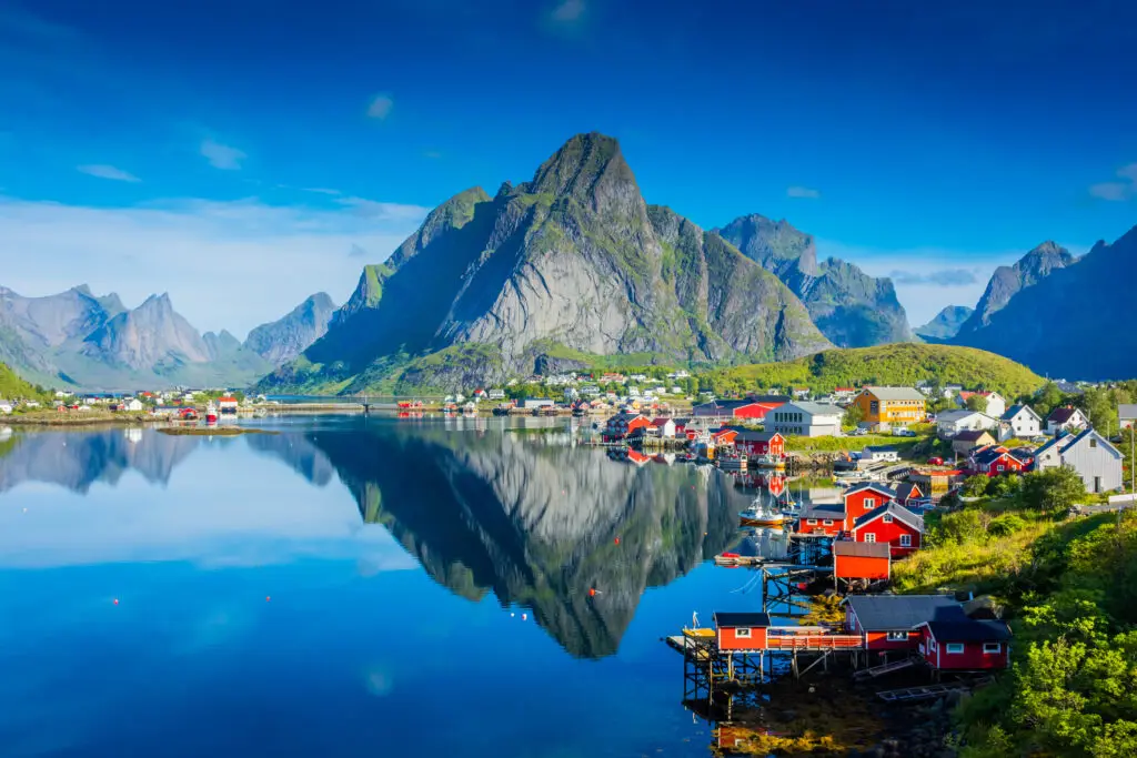 Stunning view of Reine village reflecting on the calm waters of a fjord in Lofoten Islands, Norway, highlighting vibrant houses and rugged mountains