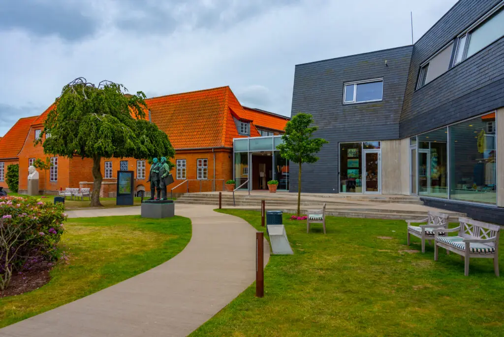 Skagens Museum in Denmark showcasing a blend of traditional and modern architecture with a sculpture in the lush garden.