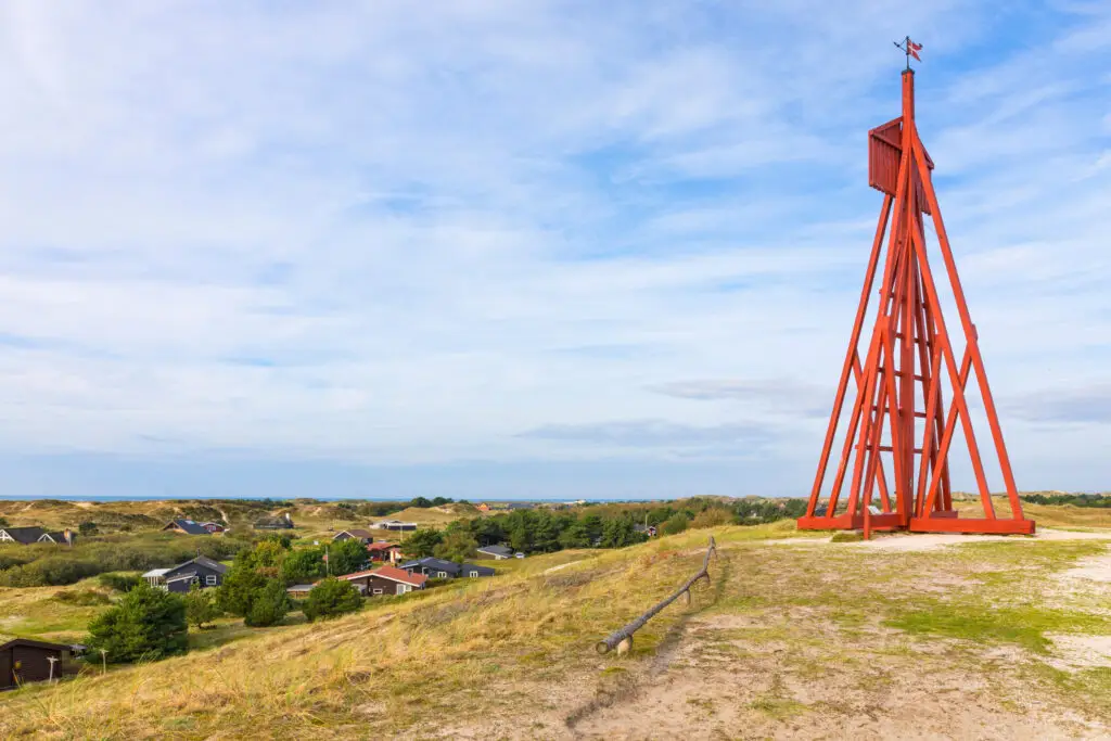 Historic red seamark towering over the dune landscape of Fanø, Denmark, with scenic views of the village and North Sea in the background.