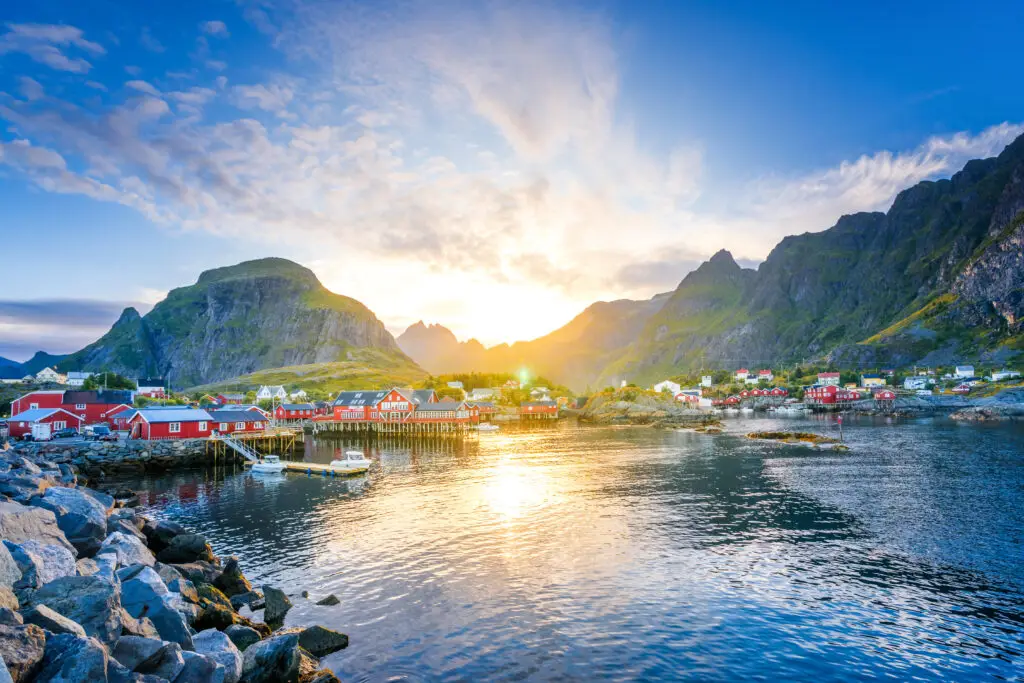 Sunset over the picturesque village of Moskenesøy in Lofoten, Norway, showing colorful houses reflected in the calm waters with dramatic mountain backdrop.