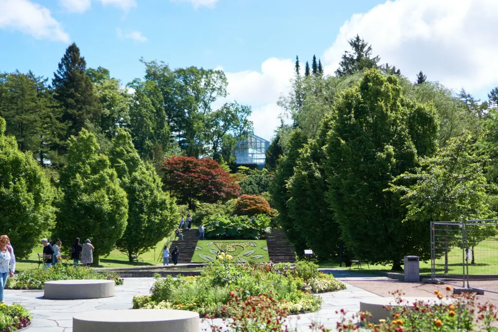 Visitors exploring the lush gardens and intricate floral designs at Gothenburg Botanical Garden in Sweden, featuring a sunlit greenhouse in the background.